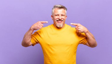 old senior man smiling confidently pointing to own broad smile, positive, relaxed, satisfied attitude