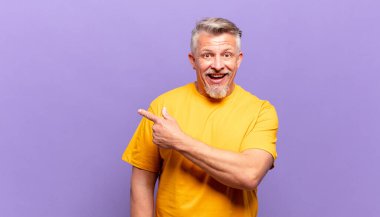 old senior man looking excited and surprised pointing to the side and upwards to copy space