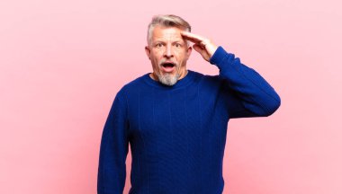 old senior man looking happy, astonished and surprised, smiling and realizing amazing and incredible good news
