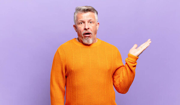 old senior man looking surprised and shocked, with jaw dropped holding an object with an open hand on the side