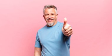 Yaşlı kıdemli adam gururlu, tasasız, kendinden emin ve mutlu, başparmağıyla olumlu gülümsüyor.