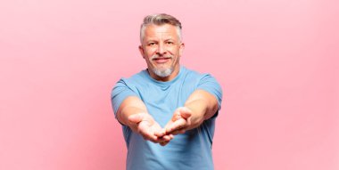 old senior man smiling happily with friendly, confident, positive look, offering and showing an object or concept