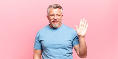 old senior man smiling happily and cheerfully, waving hand, welcoming and greeting you, or saying goodbye