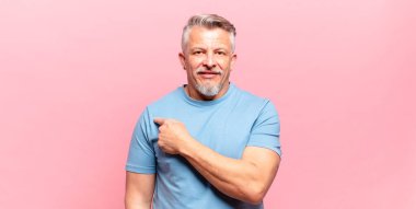 old senior man smiling cheerfully, feeling happy and pointing to the side and upwards, showing object in copy space