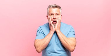 old senior man feeling shocked and scared, looking terrified with open mouth and hands on cheeks
