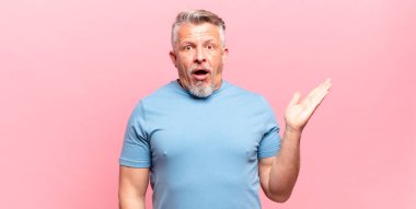 old senior man looking surprised and shocked, with jaw dropped holding an object with an open hand on the side