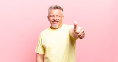 Yaşlı kıdemli adam gururlu, tasasız, kendinden emin ve mutlu, başparmağıyla olumlu gülümsüyor.