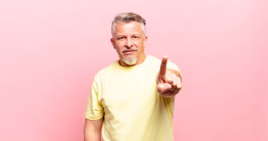 old senior man smiling proudly and confidently making number one pose triumphantly, feeling like a leader