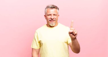old senior man smiling and looking friendly, showing number one or first with hand forward, counting down