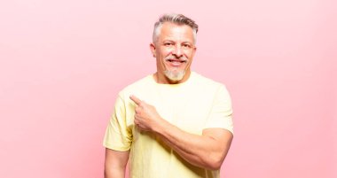 old senior man smiling cheerfully, feeling happy and pointing to the side and upwards, showing object in copy space