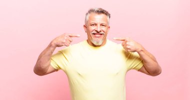 old senior man smiling confidently pointing to own broad smile, positive, relaxed, satisfied attitude