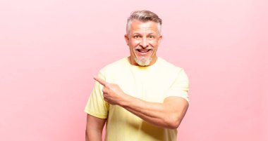 old senior man looking excited and surprised pointing to the side and upwards to copy space