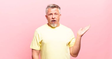 old senior man looking surprised and shocked, with jaw dropped holding an object with an open hand on the side