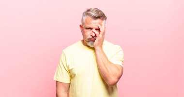 old senior man feeling bored, frustrated and sleepy after a tiresome, dull and tedious task, holding face with hand