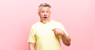 old senior man looking shocked and surprised with mouth wide open, pointing to self