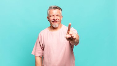 old senior man smiling proudly and confidently making number one pose triumphantly, feeling like a leader