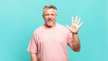 old senior man smiling and looking friendly, showing number five or fifth with hand forward, counting down