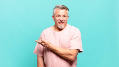 old senior man smiling cheerfully, feeling happy and showing a concept in copy space with palm of hand