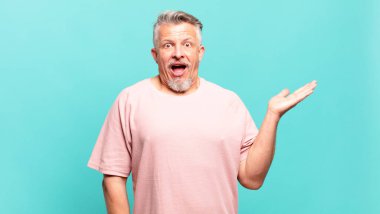 old senior man looking surprised and shocked, with jaw dropped holding an object with an open hand on the side