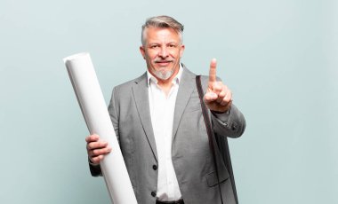 Kıdemli mimar gülümsüyor ve arkadaş canlısı görünüyor. Bir numara ya da ilk eli önde, geriye doğru sayıyor.