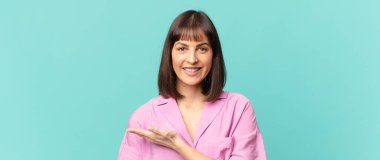 Güzel bir kadın neşeyle gülümsüyor, mutlu hissediyor ve bir konsepti fotokopi uzayında el ele vererek gösteriyor.