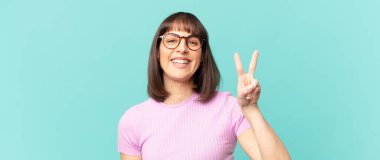 Güzel bir kadın gülümsüyor ve mutlu görünüyor, kaygısız ve pozitif, işaret eden zafer ya da barış tek elle