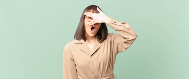 Güzel bir kadın şok olmuş, korkmuş ya da korkmuş görünüyor. Yüzü elle örtülmüş ve parmaklarının arasından gizlice bakıyor.