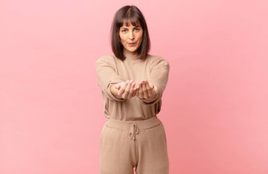 Güzel bir kadın mutlu bir şekilde gülümsüyor arkadaş canlısı, kendinden emin, pozitif bakışlı, bir nesne ya da konsept sunuyor ve gösteriyor.