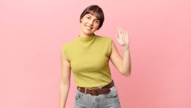 Güzel bir kadın mutlu ve neşeyle gülümsüyor, el sallıyor, seni selamlıyor ve selamlıyor, ya da hoşça kal diyor.