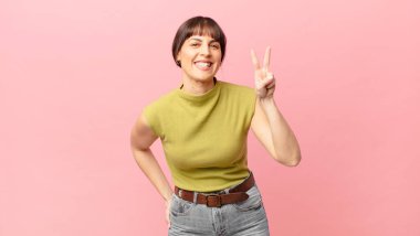 Güzel bir kadın gülümsüyor ve arkadaş canlısı görünüyor. İki ya da iki numarayı gösteriyor. Elleri önde, geri sayıyor.