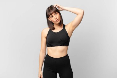 athlete woman feeling puzzled and confused, scratching head and looking to the side