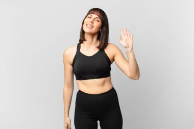 athlete woman smiling happily and cheerfully, waving hand, welcoming and greeting you, or saying goodbye