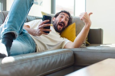 Genç sakallı adam akıllı telefonuyla kanepede dinleniyor.