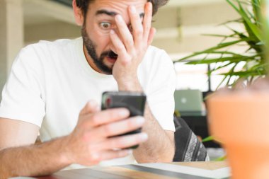 Evde akıllı telefonu olan sakallı genç bir adam.