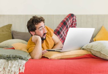 Yatakta dizüstü bilgisayarlı genç sakallı bir adam.