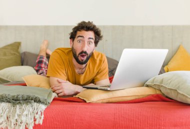 Yatakta dizüstü bilgisayarlı genç sakallı bir adam.