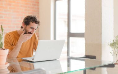 Evde dizüstü bilgisayarla çalışan sakallı genç bir adam.