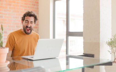 Evde dizüstü bilgisayarla çalışan sakallı genç bir adam.