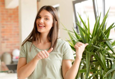 Güzel bir kadın neşeyle gülümsüyor ve yan taraftaki fotokopi alanını gösteriyor, mutlu ve tatmin olmuş hissediyor.
