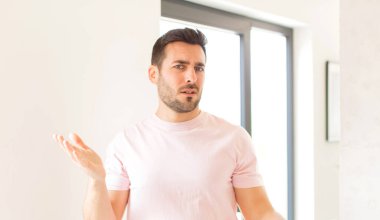 Yakışıklı adam şaşkın, kafası karışmış ve stresli görünüyor, farklı seçenekler arasında merak ediyor, kararsız hissediyor.