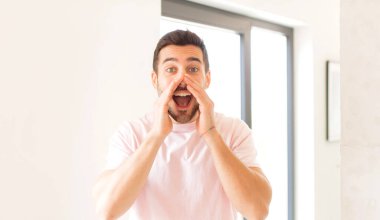 Yakışıklı adam mutlu, heyecanlı ve pozitif hissediyor. Elleri ağızda, bağırarak bağırıyor.