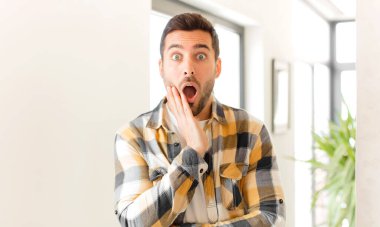 Yakışıklı adam şok ve inançsızlık içinde, elleri yanağında ve kolları çaprazlanmış, sersemlemiş ve şaşırmış hissediyor.