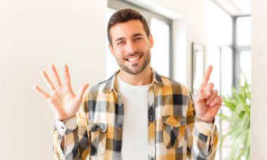 Yakışıklı adam gülümsüyor ve arkadaş canlısı görünüyor, altı ya da altıncı numarayı gösteriyor, eli önde, geri sayıyor.