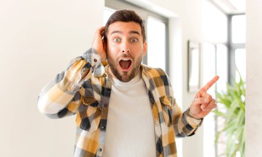 Yakışıklı adam gülüyor, mutlu, pozitif ve şaşırmış görünüyor. Yan fotokopi alanını işaret eden harika bir fikri fark ediyor.