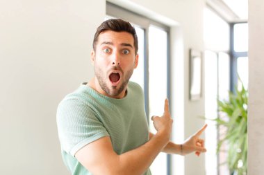 Yakışıklı adam şaşkın ve şaşırmış hissediyor, yan taraftaki fotokopi alanını işaret ediyor, şaşkın, ağzı açık bir bakışla.