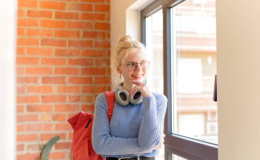 Güzel bir öğrenci mutlu ve kendinden emin bir ifadeyle gülümsüyor, elleri çenesinde, merak ediyor ve yan tarafa bakıyor.
