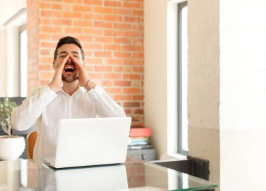 Yakışıklı iş adamı mutlu, heyecanlı ve pozitif hissediyor. Elleri ağızda, bağırarak bağırıyor.