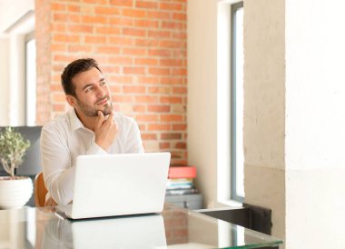 Yakışıklı iş adamı mutlu, kendinden emin bir ifadeyle gülümsüyor, elleri çenesinde, merak ediyor ve yan tarafa bakıyor.