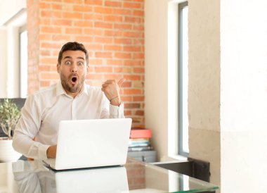 Yakışıklı işadamı, inançsızlıktan şaşkın şaşkın bakıyor, yan taraftaki objeyi işaret ediyor ve 