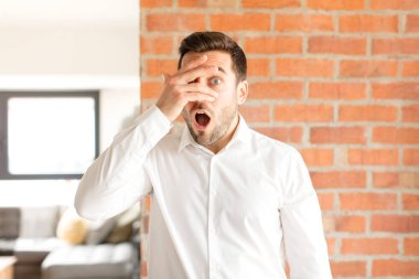 Yakışıklı iş adamı, şok olmuş, korkmuş ya da korkmuş görünüyor. Yüzü elle kaplanmış ve parmaklarının arasından gizlice bakıyor.